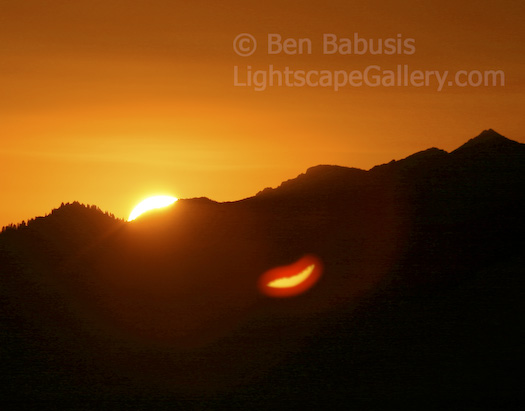 Sun Smile. Evergreen Mountain, Washington. The sun rises in the central Cascades. Interestingly, the partially risen sun reflects off of elements in the lens creating a lens flare which looks eerily like smiling lips.  Ben Babusis, Lightscape Gallery.